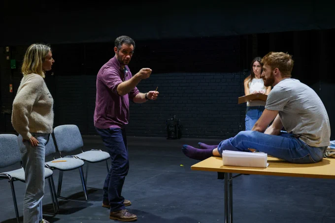 Photo from The Commotion Time rehearsals: Chloe Endean, Ben Callon and Lizzy Watts watch director Martin Berry as he demonstrates a scene with his arms held in front of him. 